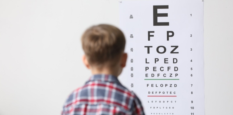 A young boy looking at a Snellen chart at the eye doctor’s office.