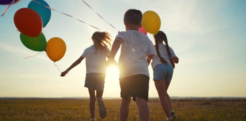 A group of kids are running around in nature with balloons.