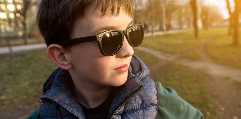 A young boy outside wearing a pair of black, tinted glasses.