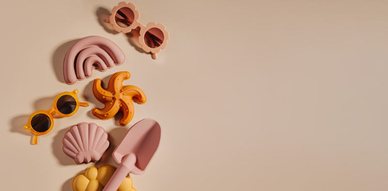 A flat lay composition of two pairs of colorful sunglasses, seashells and a spade in orange and pink.