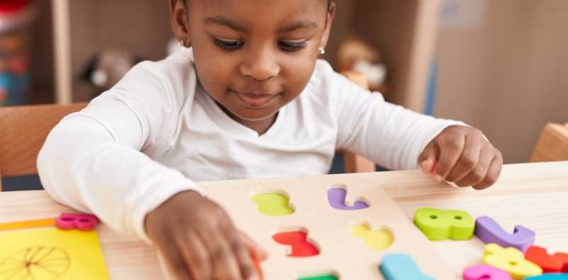 A toddler playing with number shapes on a wooden table in a playroom