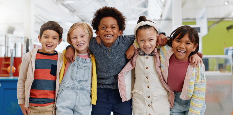 A group of children from different ethnic backgrounds hugging at school.