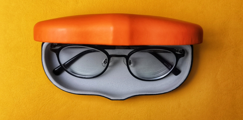 Black eyeglasses in an orange case on an orange background, illustrating proper glasses storage