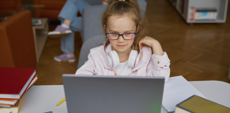 A young girl wearing glasses and completing homework on a laptop