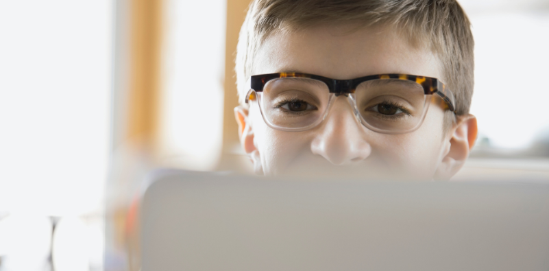 A young boy wearing tortoiseshell glasses using a laptop