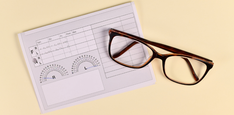 A pair of brown eyeglasses on top of a paper eyeglasses prescription