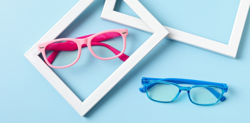 A pair of pink eyeglasses and a pair of blue eyeglasses against a blue background with whit photoframes positioned around the eyewear