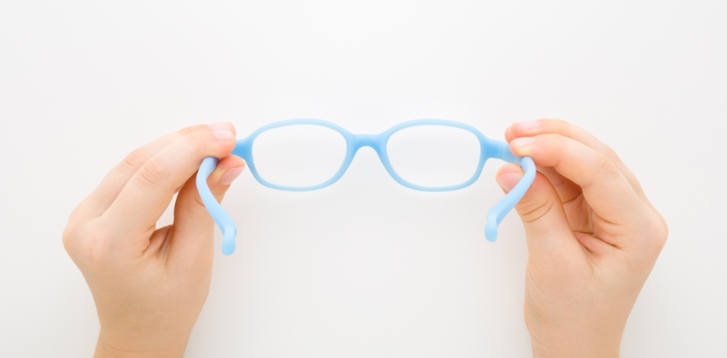 A young child’s hands, holding a pair of blue eyeglasses against a white background