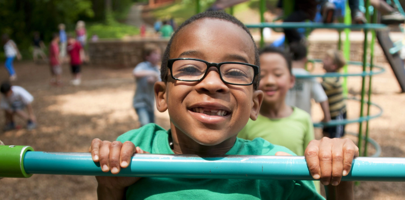 Child wearing kids' glasses while playing outdoors at a playground.