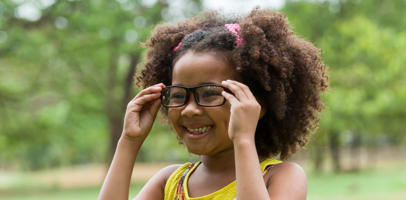Smiling child adjusting their kids' glasses outdoors.