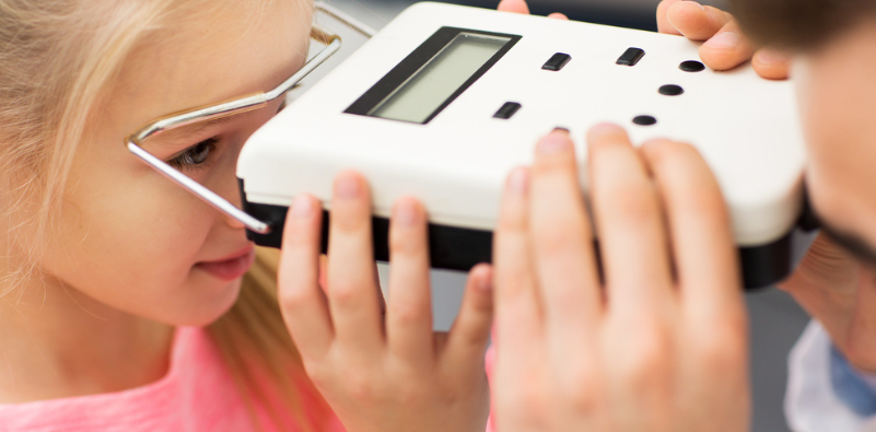 Optician using a pupillometer to measure a child’s eyes for glasses fitting.]